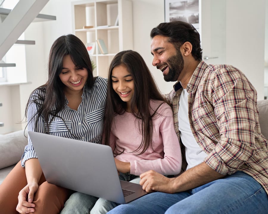 Une jeune famille composée d'une femme, d'un homme et d'un jeune adolescent est assise ensemble sur un canapé en regardant un ordinateur portable.